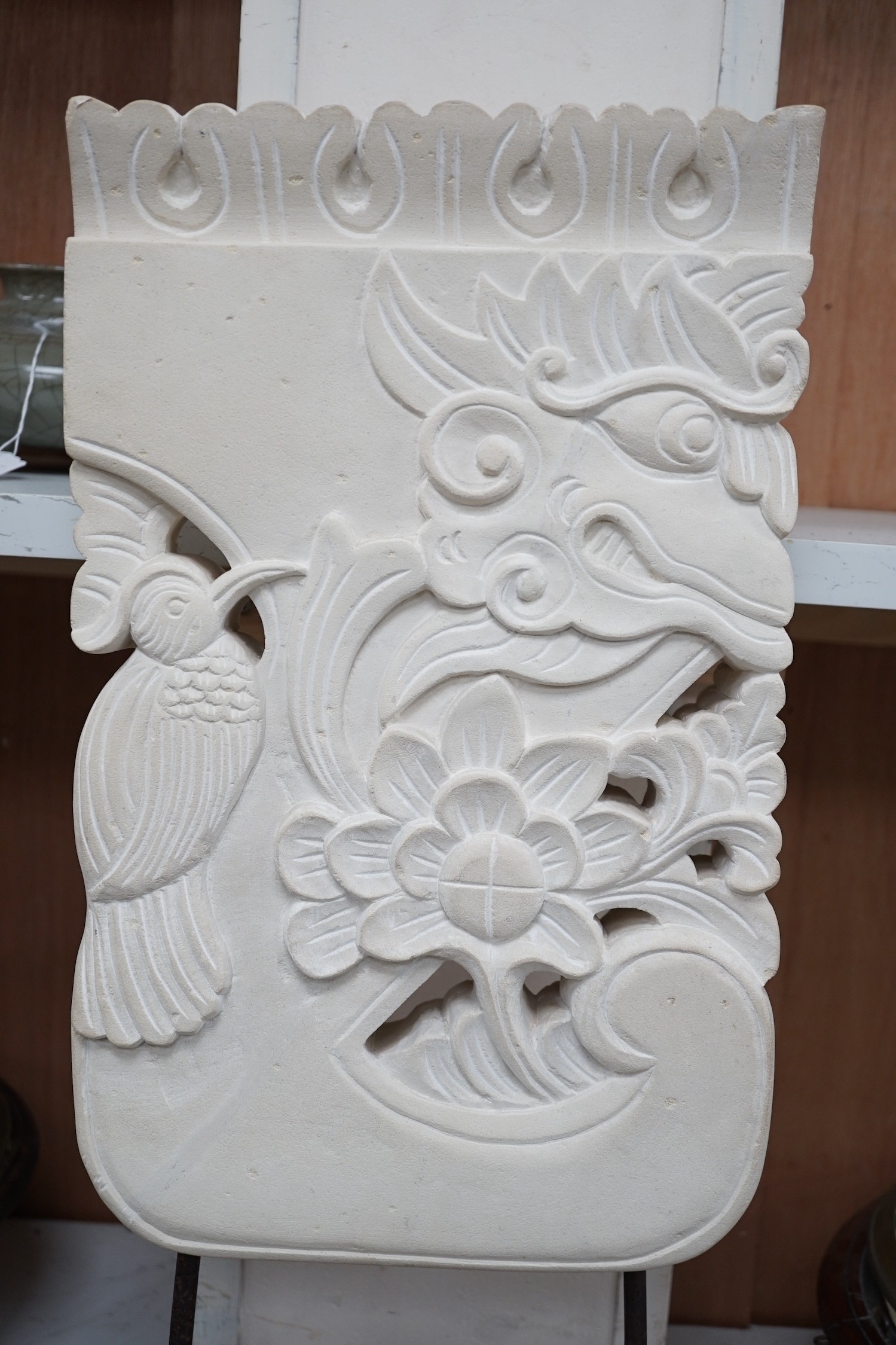 An Indonesian sandstone carving of a mask, bird and flowers on hardwood stand, 62.5cms high Height 63 cm.